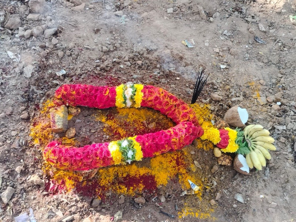 Premium grave decorated with thick horseshoe-shaped rose garland, incense sticks and fruit offerings